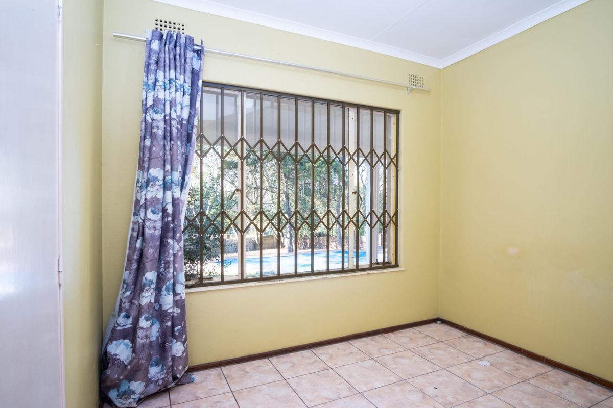An empty bedroom featuring tiled flooring, a window with a security gate, and neutral wall paint.