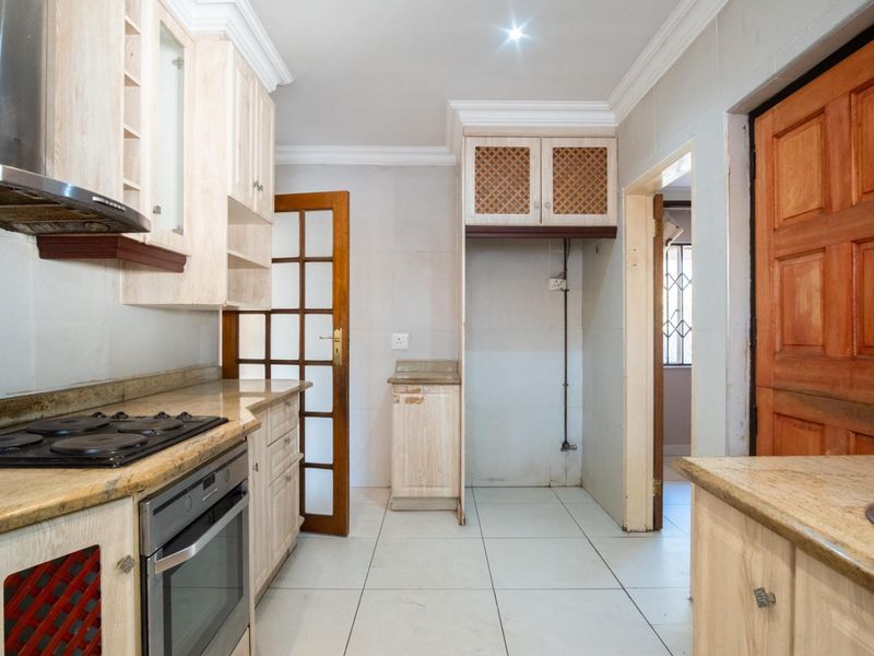 A functional kitchen featuring light wood cabinetry, granite countertops, built-in oven, gas hob, and tiled flooring, offering a clean space ready for updates.