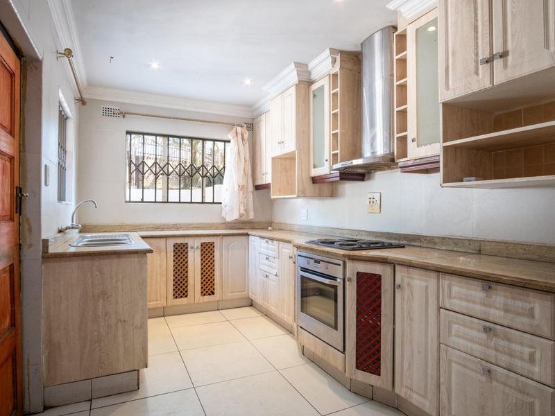 A functional kitchen featuring light wood cabinetry, stone countertops, built-in oven, electric hob, and stainless steel extractor fan with tiled flooring.