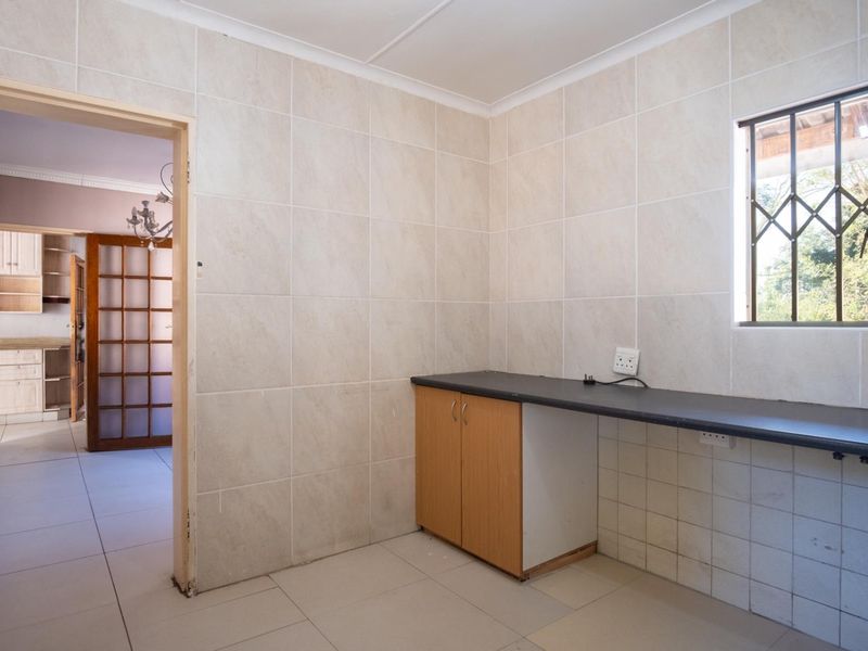 A functional scullery or utility area featuring tiled walls, built-in cabinetry with a laminate countertop, and a window with a security gate.