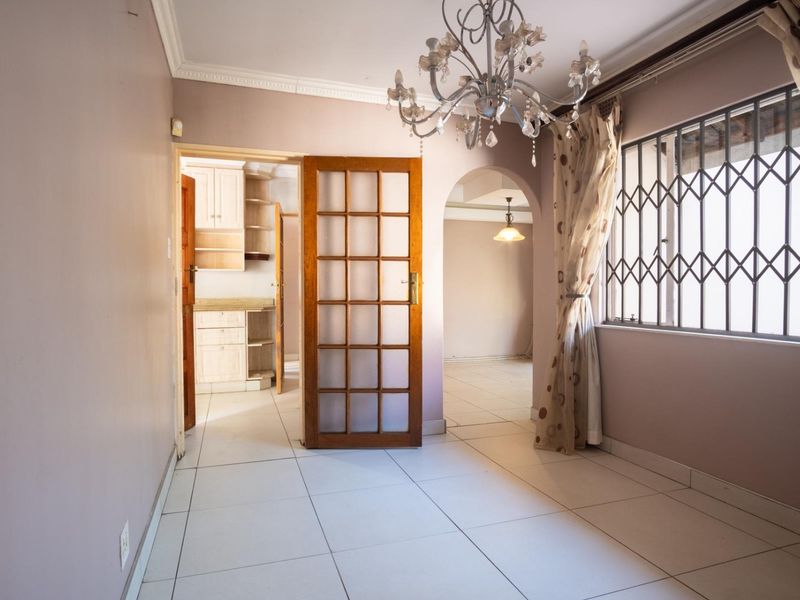 A bright, empty living area featuring tiled floors, crown molding, and an arched entryway leading to an adjacent space with a view of the kitchen.