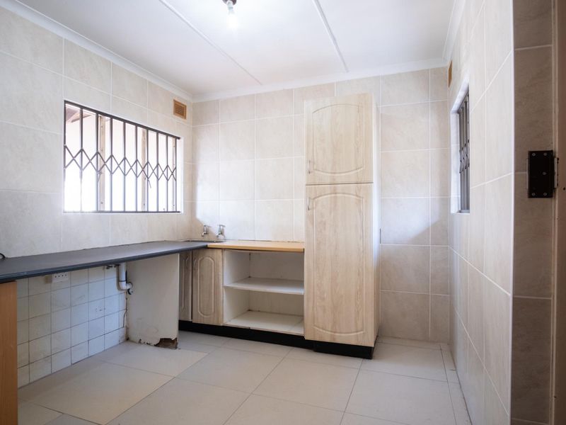 A functional kitchen space featuring tiled walls and floors, built-in cabinetry, and security bars on the windows, currently awaiting updates and finishing touches.