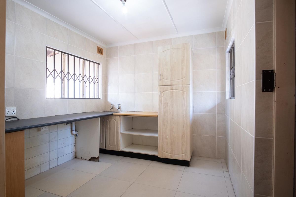 A functional kitchen space featuring tiled walls and floors, built-in cabinetry, and security bars on the windows, currently awaiting updates and finishing touches.