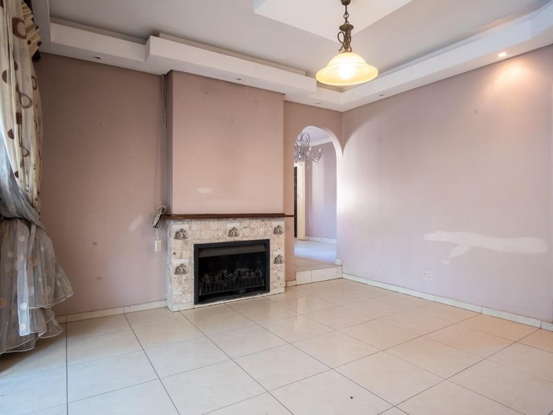 An empty living room featuring a built-in fireplace, tiled flooring, and a decorative recessed ceiling with an arched entryway.