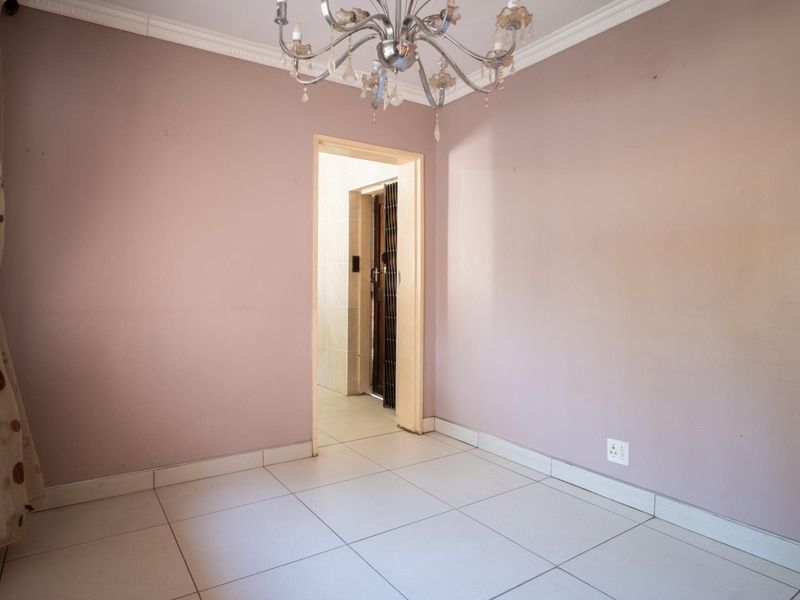 An empty living area featuring neutral tiled flooring, decorative ceiling cornice, and a central chandelier, providing a blank canvas for interior design.