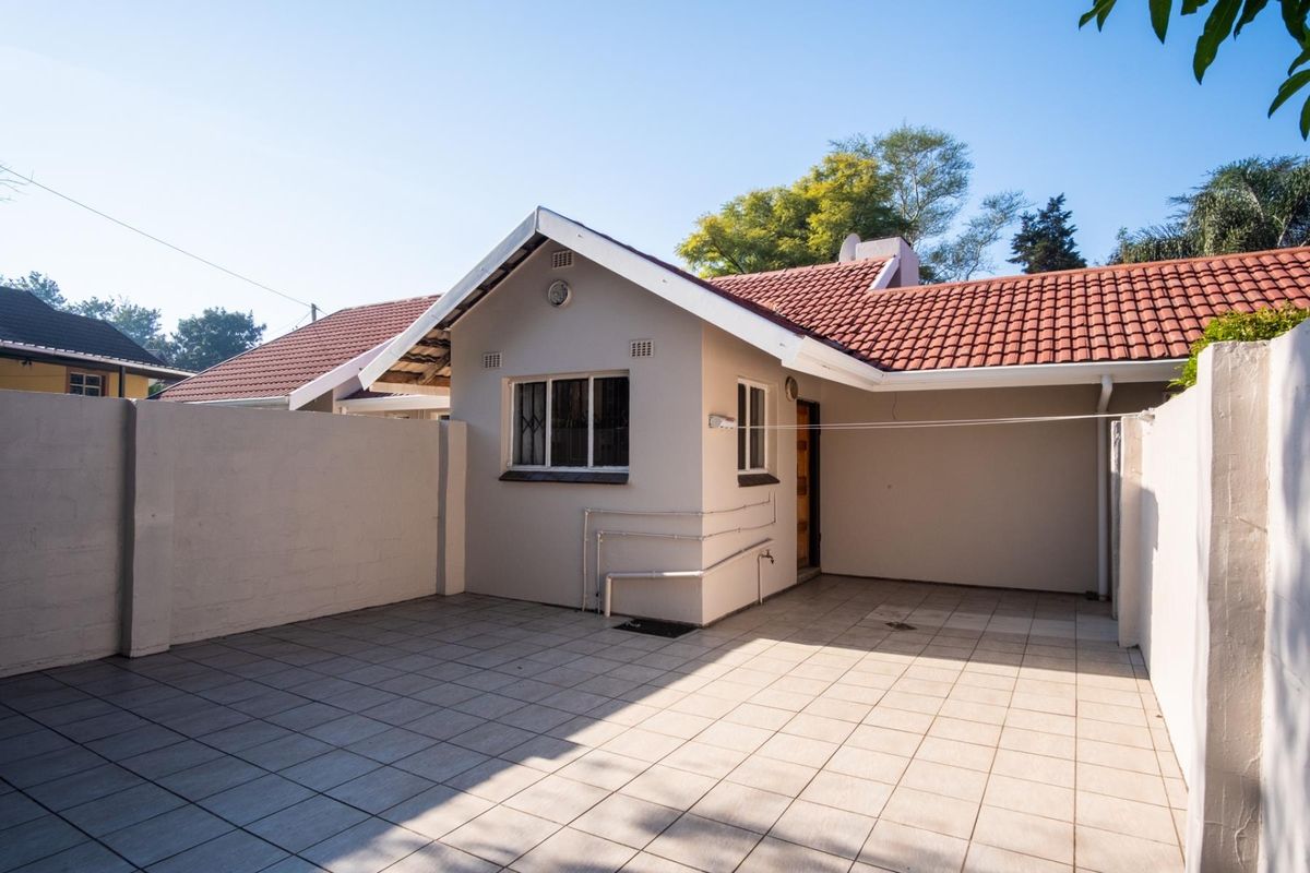A clean and well-maintained rear exterior area featuring a paved patio, perimeter walling, and a tiled roof structure.