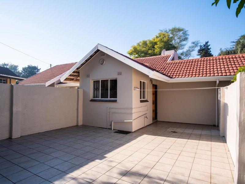 A clean and well-maintained rear exterior area featuring a paved patio, perimeter walling, and a tiled roof structure.