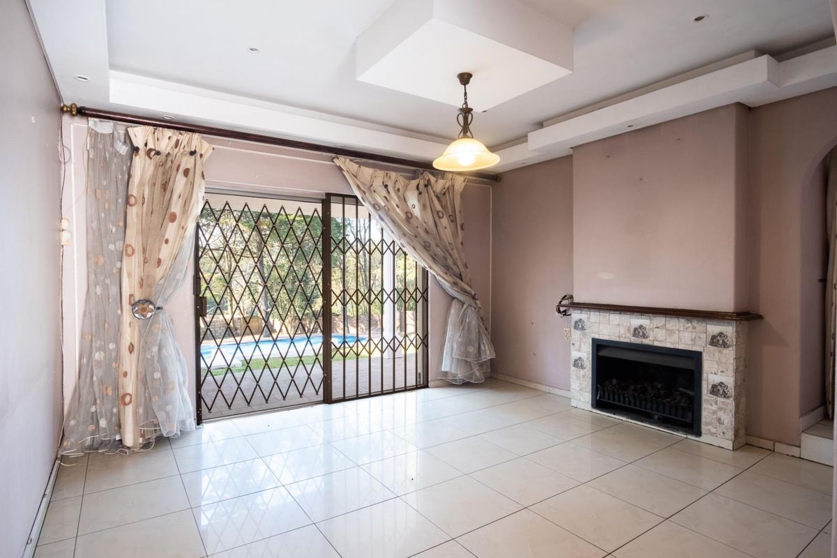 Spacious living room featuring tiled flooring, a built-in fireplace, and sliding glass doors with security gates leading to the pool area.