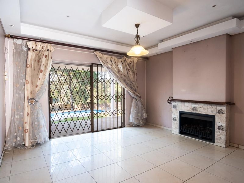 Spacious living room featuring tiled flooring, a built-in fireplace, and sliding glass doors with security gates leading to the pool area.
