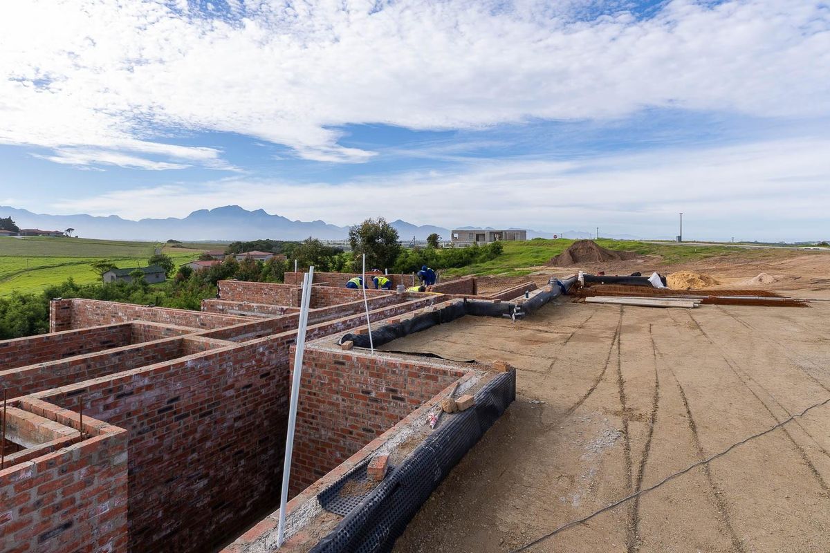 An elevated view of a residential property under construction, showing brick wall foundations and site preparation with scenic mountain views in the background.