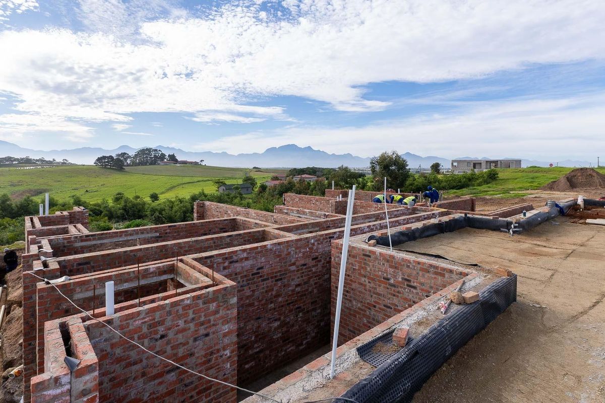 Construction site showing the brickwork foundation and wall structure of a new house with scenic mountain views in the background.