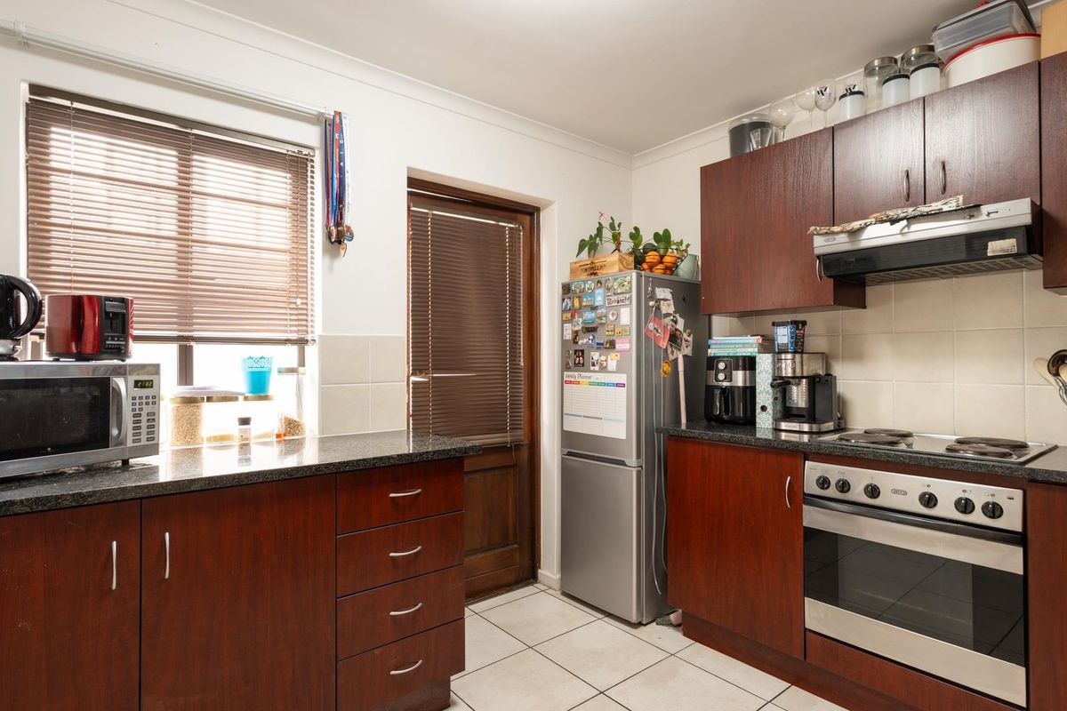 A functional kitchen featuring dark wood cabinetry, granite countertops, built-in oven, electric hob, and tiled flooring with direct access to the exterior.