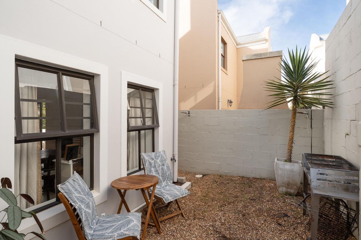 A private rear courtyard featuring gravel ground cover, a cinder block boundary wall, and access to the interior via casement windows.