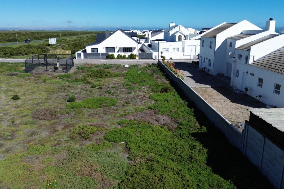 Aerial view of a vacant residential plot featuring natural vegetation, a boundary wall, and adjacent paved driveway access.