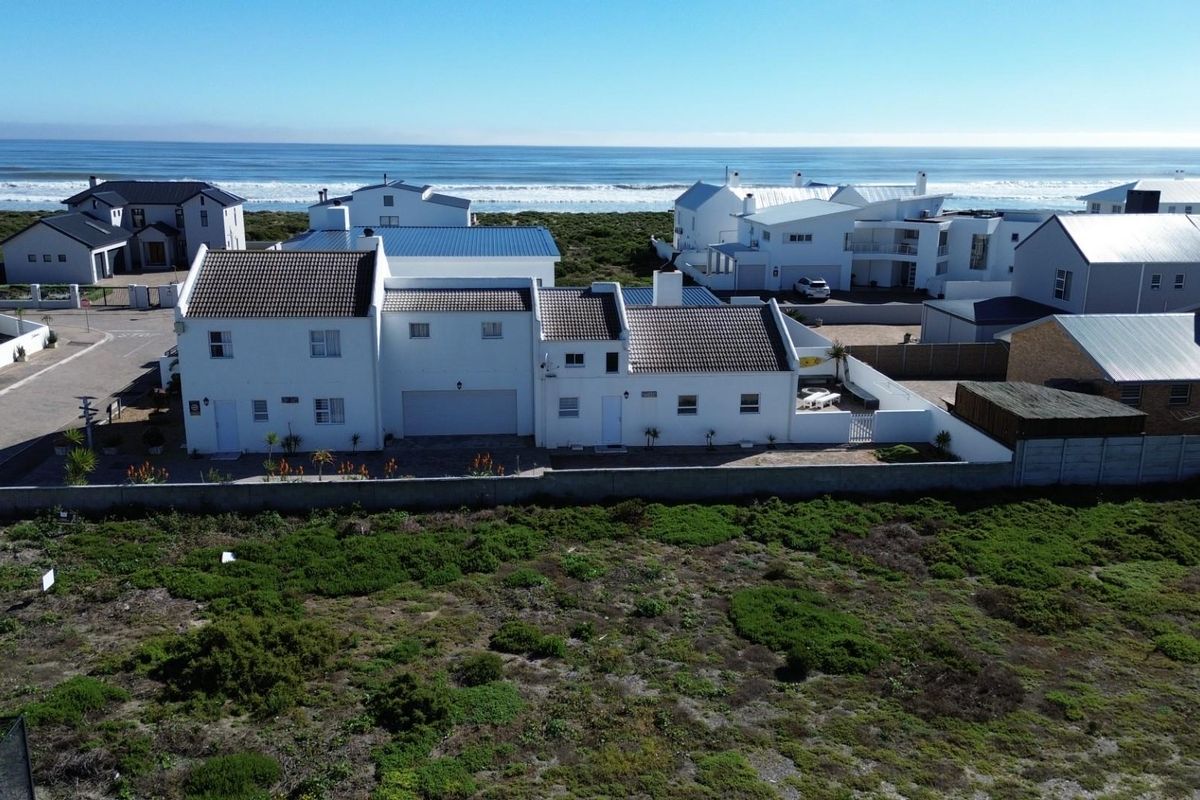 Aerial view of a residential property featuring a tiled roof, boundary wall, and paved driveway, situated in a coastal neighborhood near the ocean.