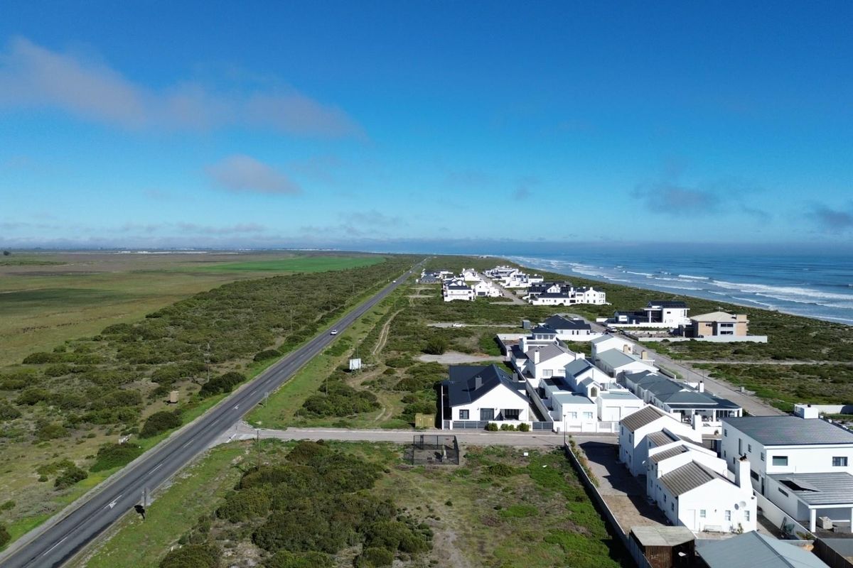 An aerial view of a coastal residential estate situated between a main road and the ocean, showcasing the surrounding natural landscape.