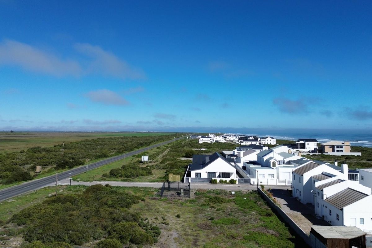 Aerial view of a coastal residential area featuring a paved road, surrounding natural vegetation, and proximity to the ocean.