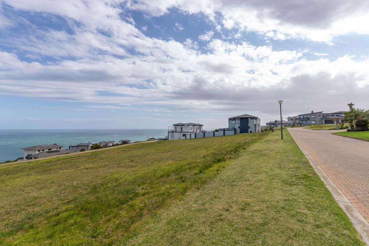 A vacant residential plot featuring expansive ocean views, adjacent to a paved street in a coastal estate setting.