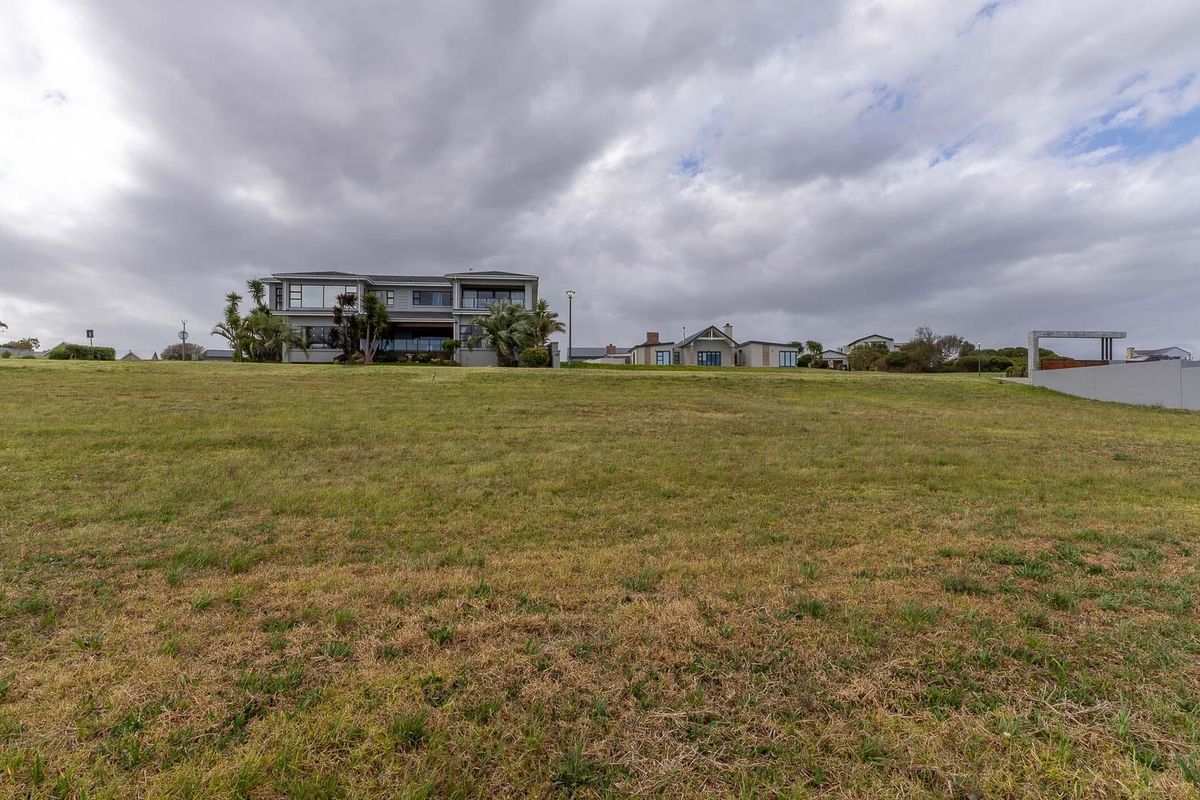 A wide-angle view of a vacant residential plot featuring a grass lawn with neighbouring properties visible in the background.