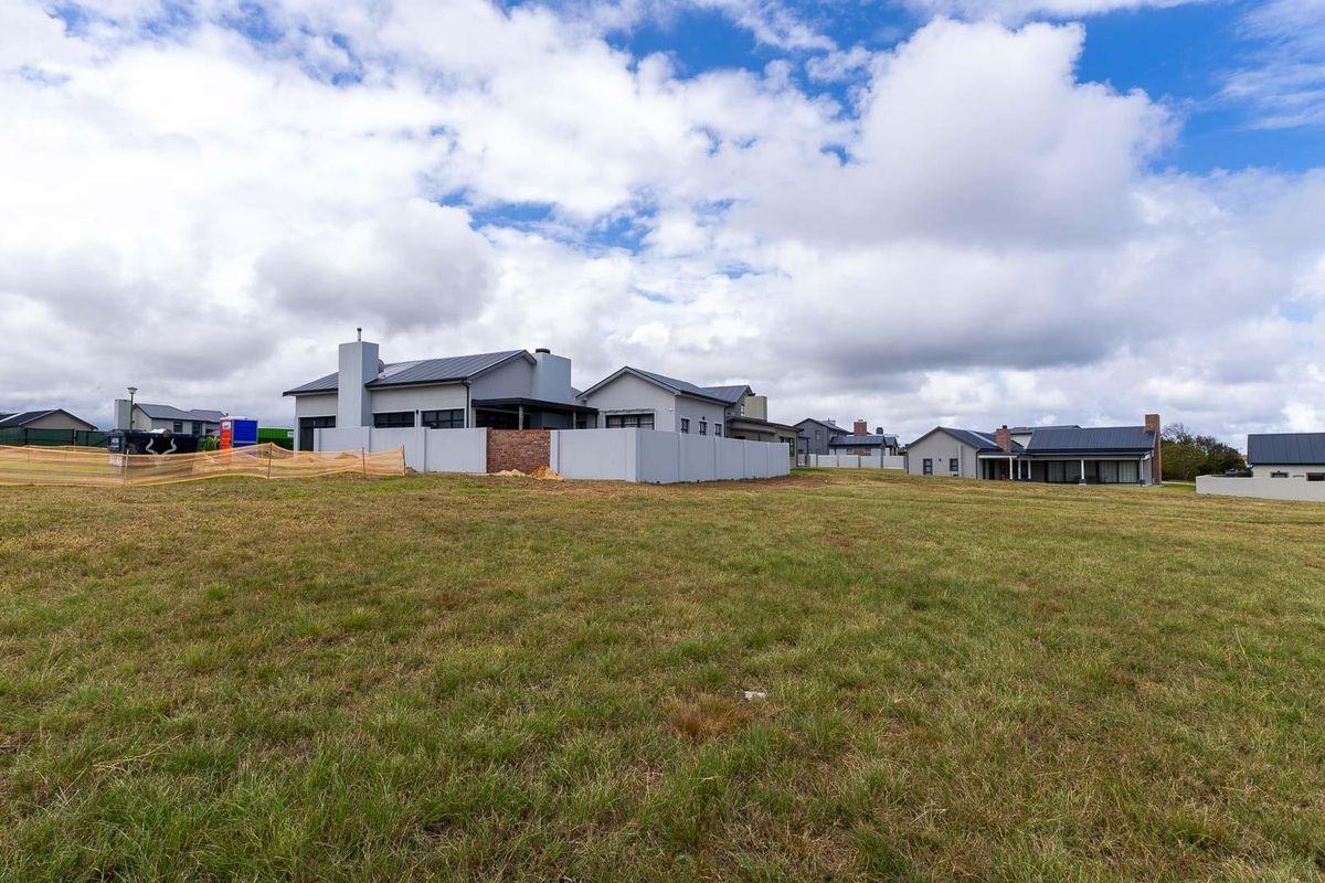 A view of a vacant residential plot with established boundary walls and surrounding neighborhood homes under a cloudy sky.