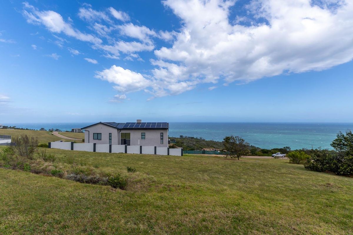 A rear view of a modern residential property featuring solar panels on the roof, set against a scenic coastal landscape.