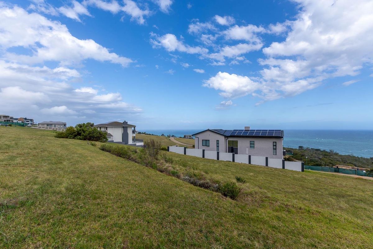 A view of a residential property featuring a grass lawn, boundary wall, and solar panels installed on the roof, overlooking the ocean.