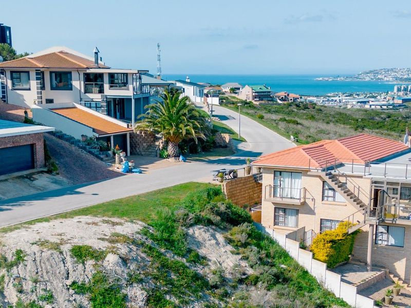 Aerial view of a coastal residential neighborhood featuring multi-level homes, paved streets, and scenic ocean views.