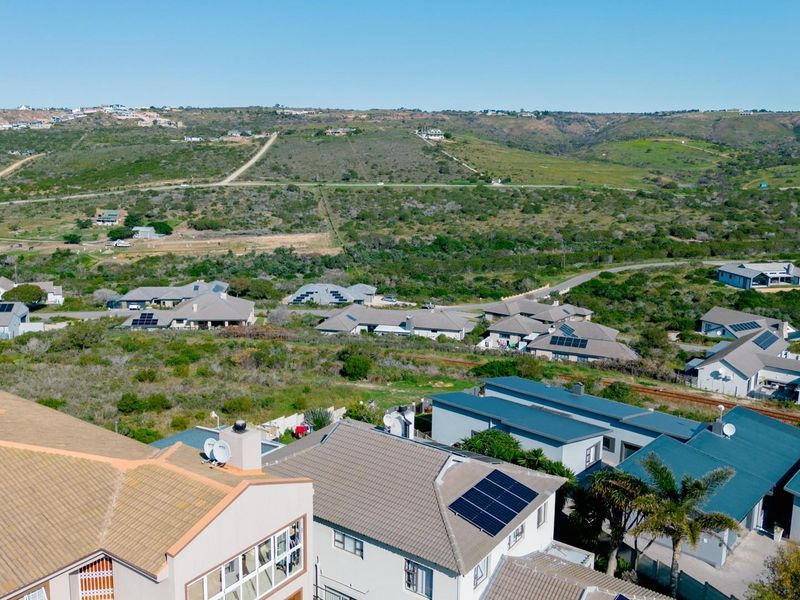 An aerial view of a residential estate featuring multiple homes with tiled roofs and solar panel installations set against a natural landscape.