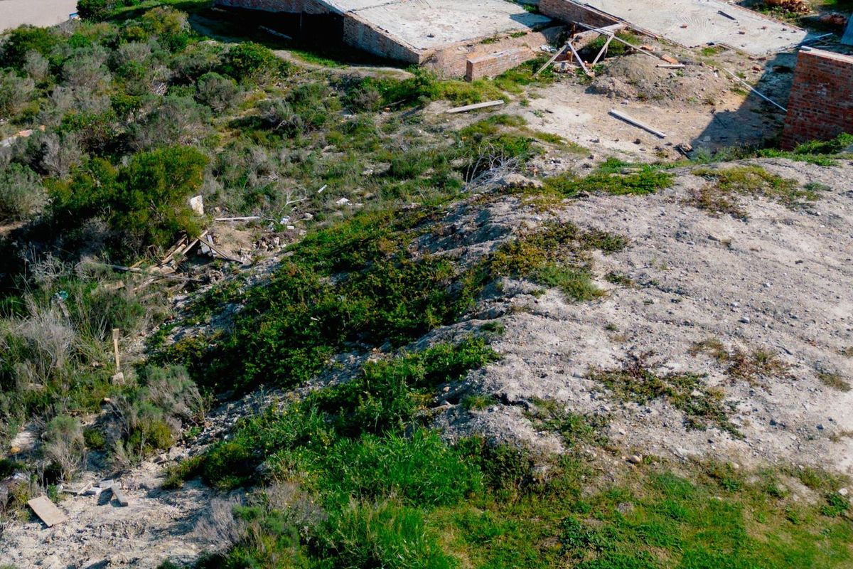 Aerial view of a vacant residential plot featuring native vegetation and the foundation of an unfinished brick structure.
