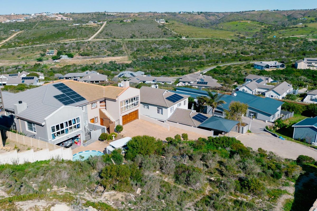 Aerial view of a residential property featuring solar panels, a swimming pool, and a paved driveway within a suburban estate setting.