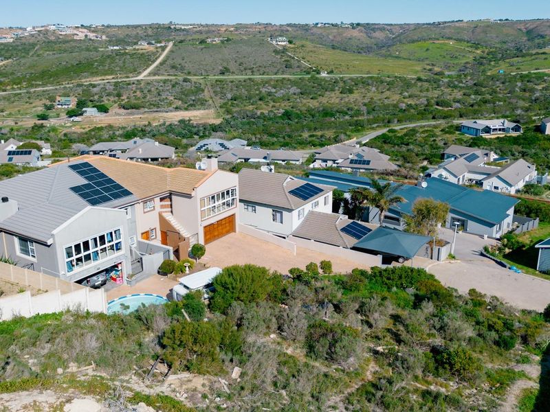 Aerial view of a residential property featuring solar panels, a swimming pool, and a paved driveway within a suburban estate setting.