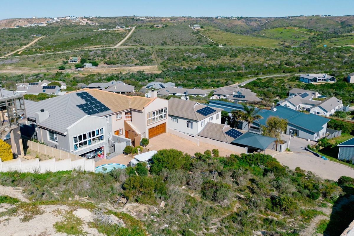 Aerial view of a residential property featuring solar panels, a swimming pool, and a paved driveway within a suburban estate setting.