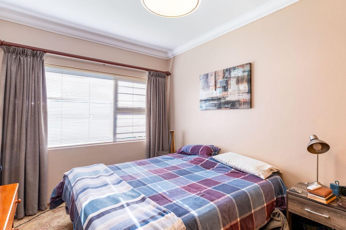 A well-lit bedroom featuring neutral wall tones, crown molding, and window blinds, providing a comfortable and functional living space.