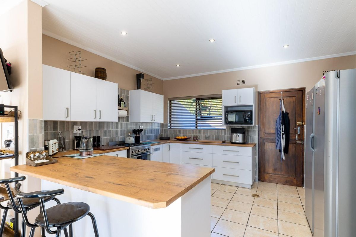 A functional kitchen featuring white cabinetry, warm wooden countertops, tiled backsplash, and neutral floor tiles, offering a clean and practical workspace.