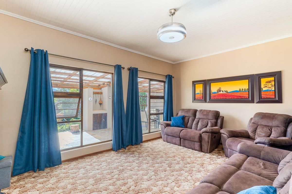 A spacious living room featuring large aluminium windows with direct access to an outdoor patio area and a classic tongue and groove ceiling.