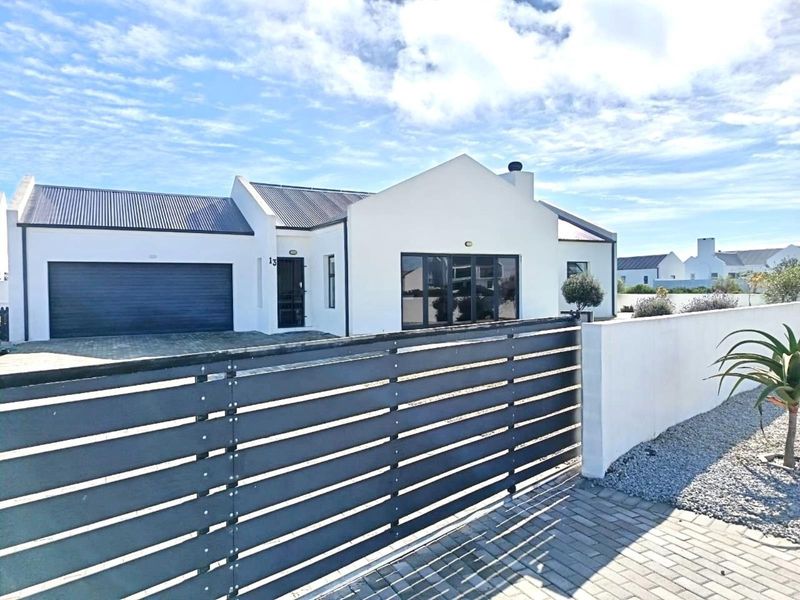 Modern single-story residence featuring a clean white facade, corrugated metal roof, paved driveway, and secure gated entrance.