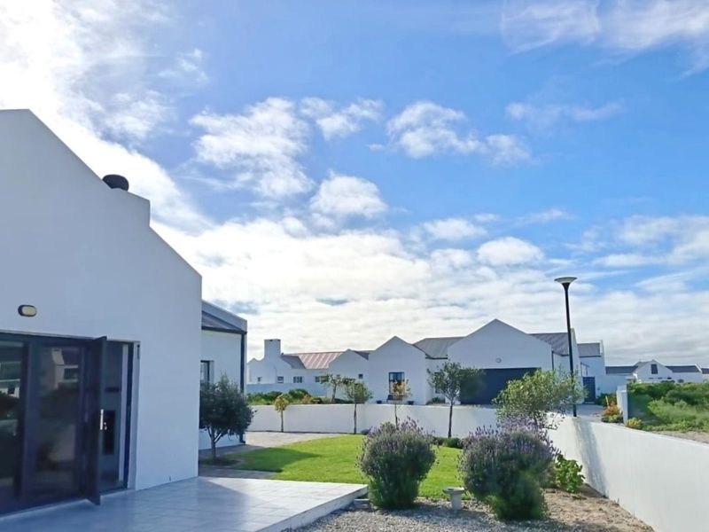 A well-maintained rear exterior view featuring a tiled patio, landscaped garden, and boundary wall within a modern residential estate.