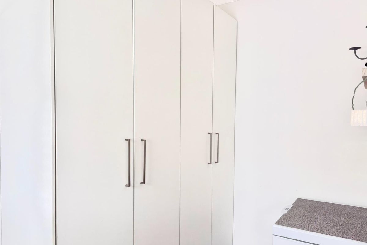 A clean, minimalist bedroom space featuring modern white built-in cupboards with sleek metal handles.
