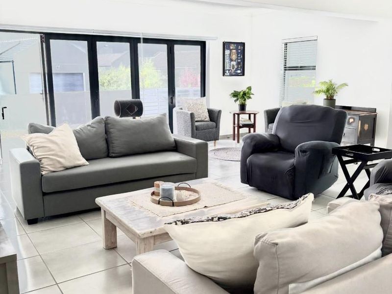Spacious living room featuring light-colored tiled flooring, vaulted ceilings with exposed beams, and large black aluminium bifold doors providing ample natural light.