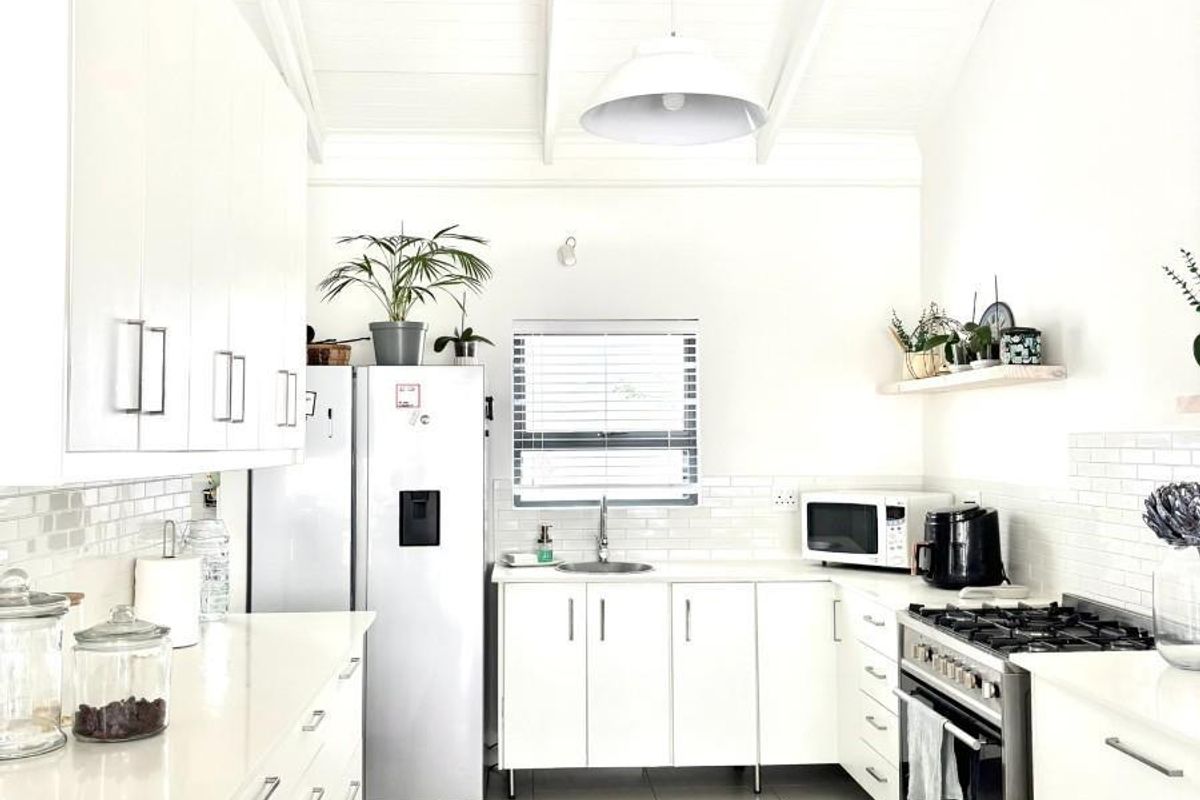 Modern, bright kitchen featuring white cabinetry, stone countertops, subway tile backsplash, gas stove, and high vaulted ceilings with exposed beams.