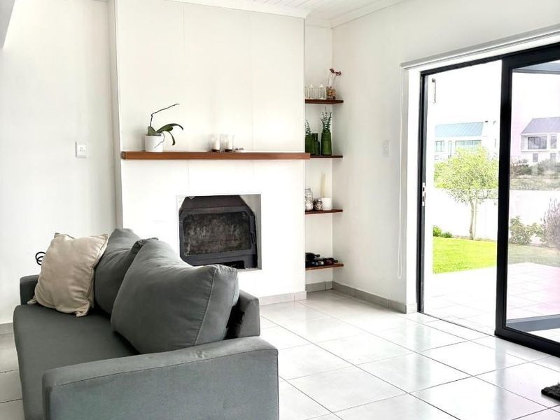 Bright living room featuring a built-in fireplace with timber mantel, recessed shelving, tongue and groove ceiling, and large sliding doors opening to the garden.