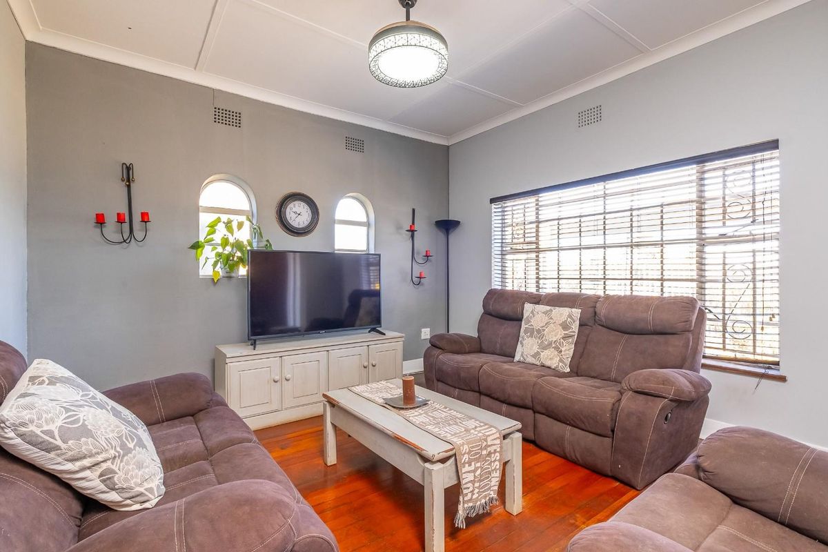 A comfortable living room featuring polished hardwood flooring, arched windows, and classic ceiling cornicing, providing a warm and inviting atmosphere.