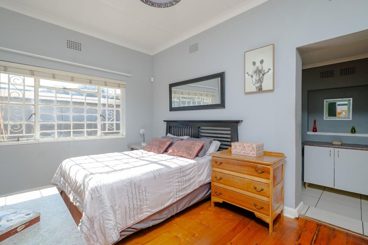A bedroom featuring hardwood flooring, security bars on the window, and an adjoining alcove with built-in cabinetry.