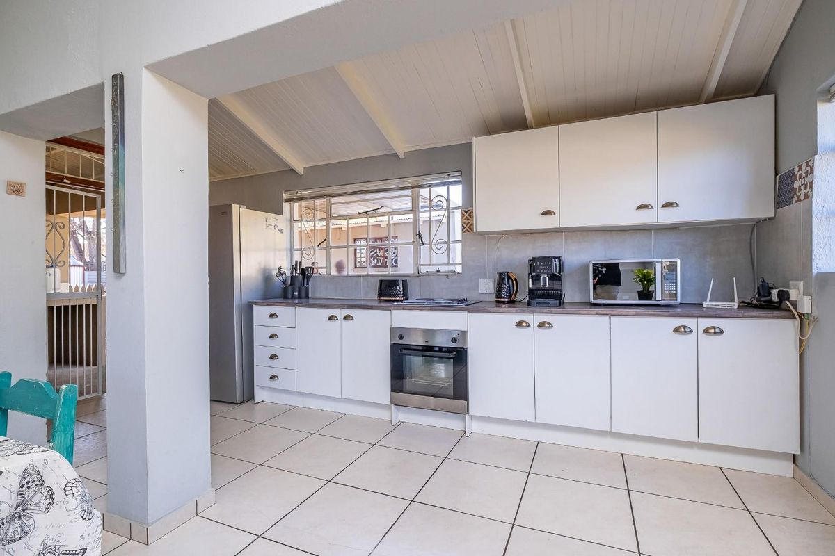 A functional kitchen featuring white cabinetry, laminate countertops, built-in oven, hob, and tiled flooring, with a view through to an adjacent outdoor area.