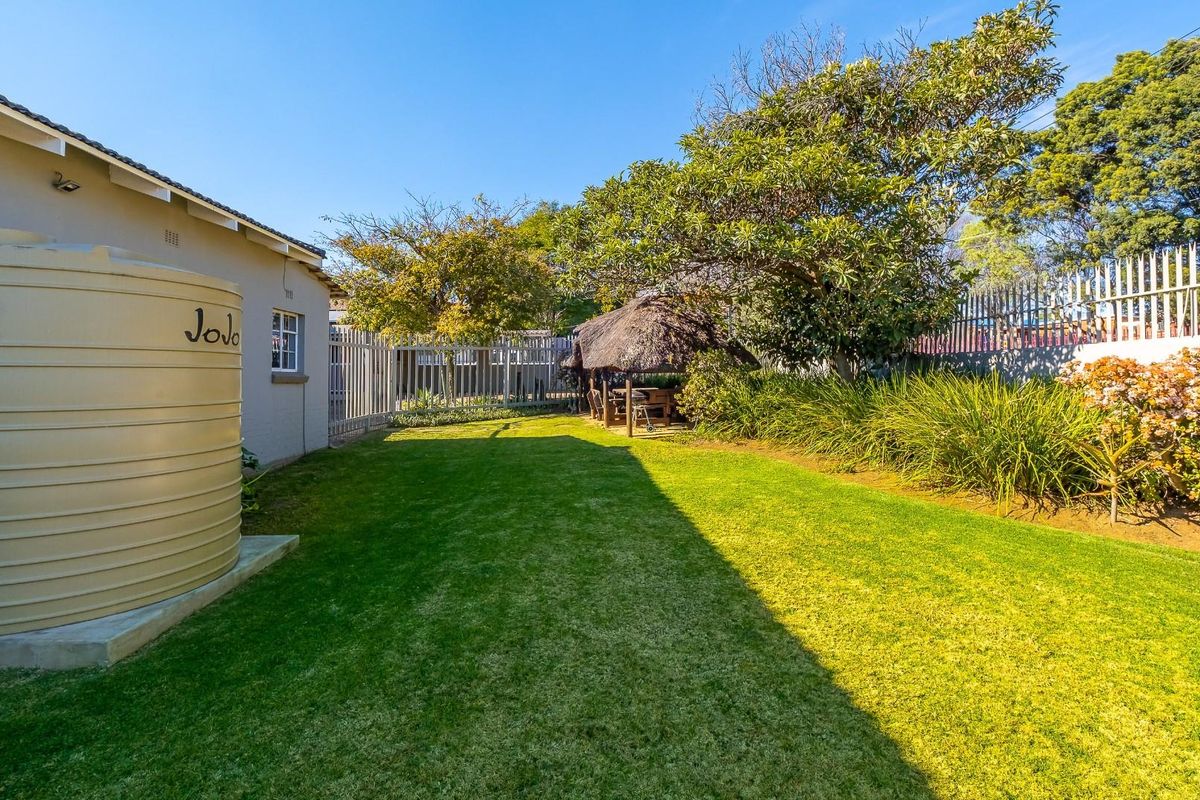 A well-maintained rear garden featuring a lush lawn, a thatched lapa for outdoor entertaining, and a large water storage tank.