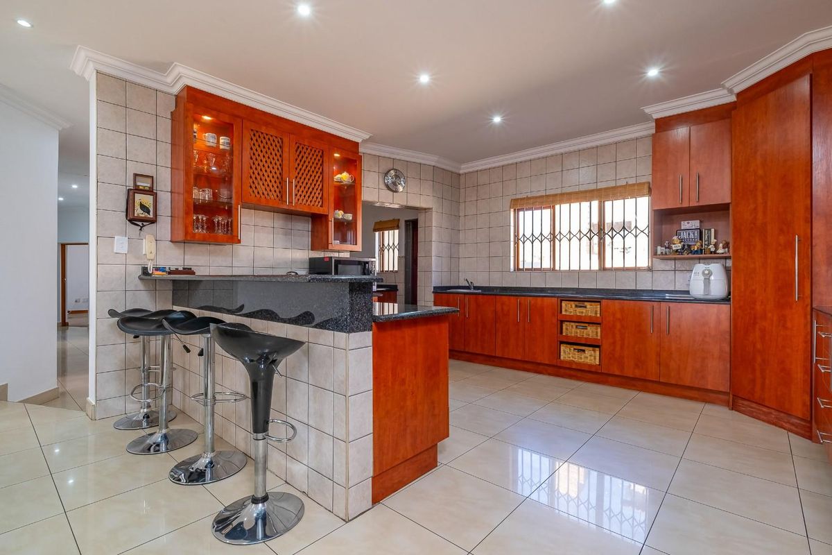 Spacious kitchen featuring warm wooden cabinetry, granite countertops, a breakfast bar, and tiled flooring, offering a functional and well-maintained cooking space.