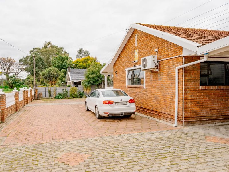 Front exterior view of a brick house featuring a paved driveway, carport, and secure boundary walling.