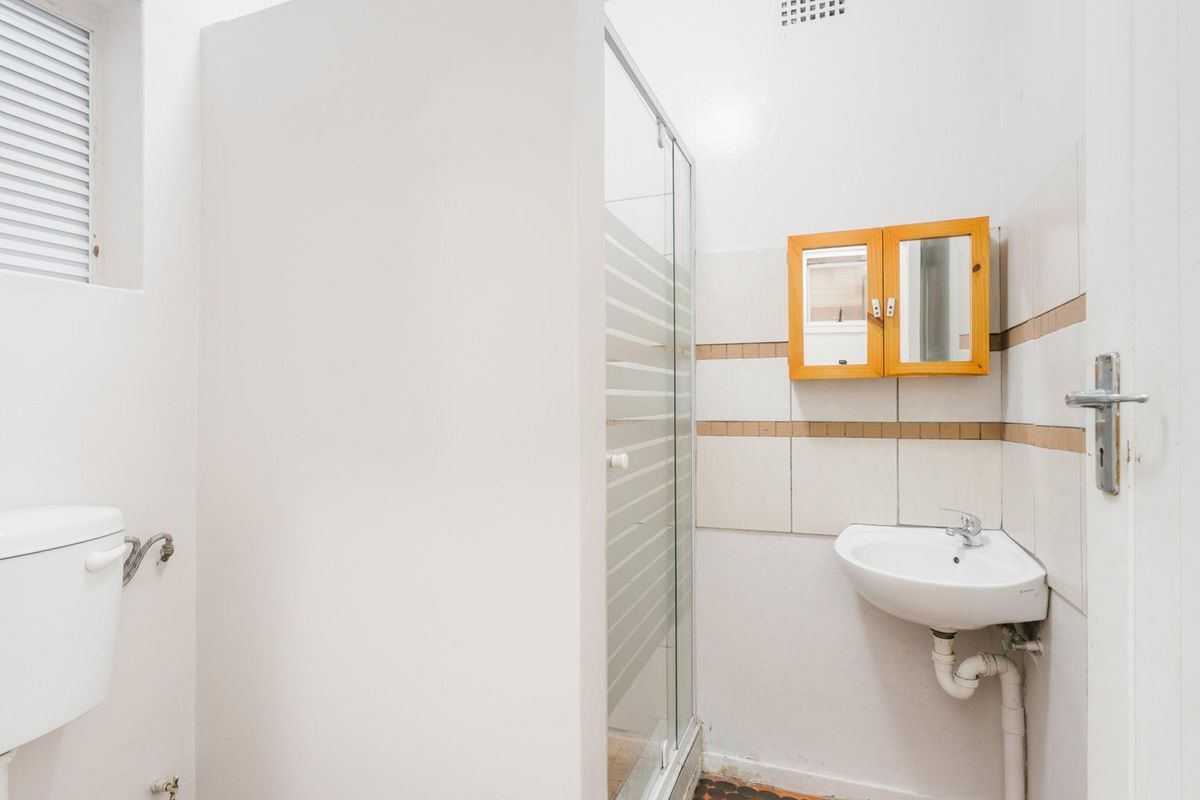 A functional bathroom featuring a shower enclosure, wall-mounted basin, and toilet, with dated tiling and exposed plumbing fixtures.