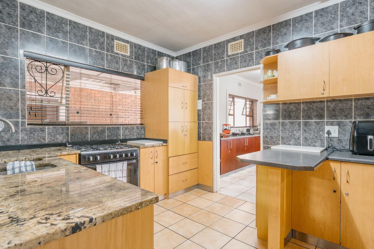 A functional kitchen featuring granite countertops, light wood cabinetry, gas stove, and tiled finishes, with an adjacent scullery area visible through the doorway.