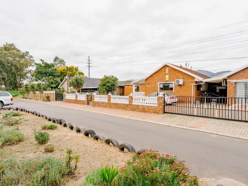Front view of a brick-faced residential property featuring a secure metal gate, paved driveway, and boundary wall.